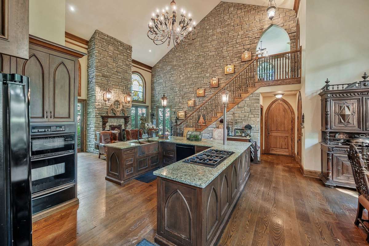 Kitchen cabinetry is crafted with elegant arched panels. The rugged stone wall lined with sconces provides a warm unexpected contrast to the beauty of both materials.  The kitchen is both a functional space and a experience of historic cozy warmth.