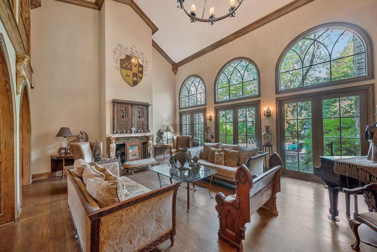 Step into the grand Gothic great room where soaring arched openings frame the space and tall arched windows line the back wall flooding natural light into the room and offering enchanting views of the secluded pool surrounded by towering trees