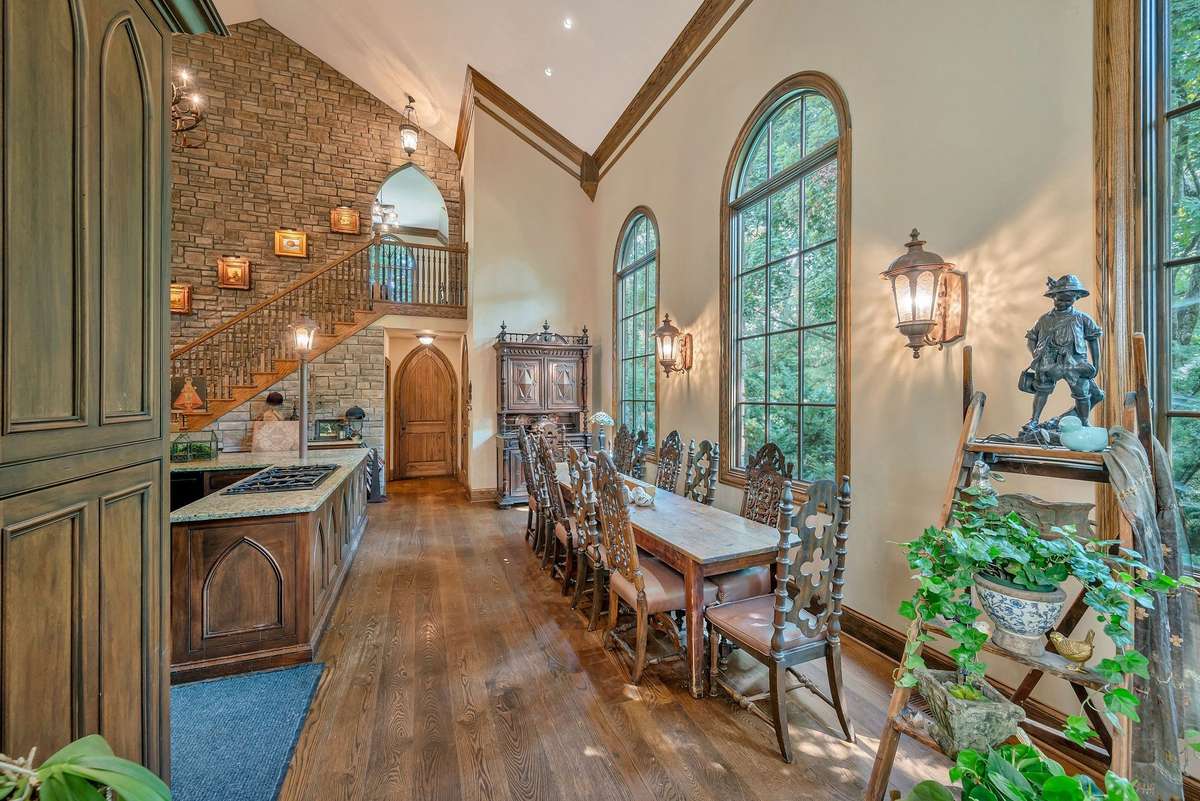 This kitchen feels like a grand timeless hall history and hearth converge. Tall vaulted two story ceiling, arch paneling and stone wall with sconces lighting art pieces that lead to the media room up the stairs