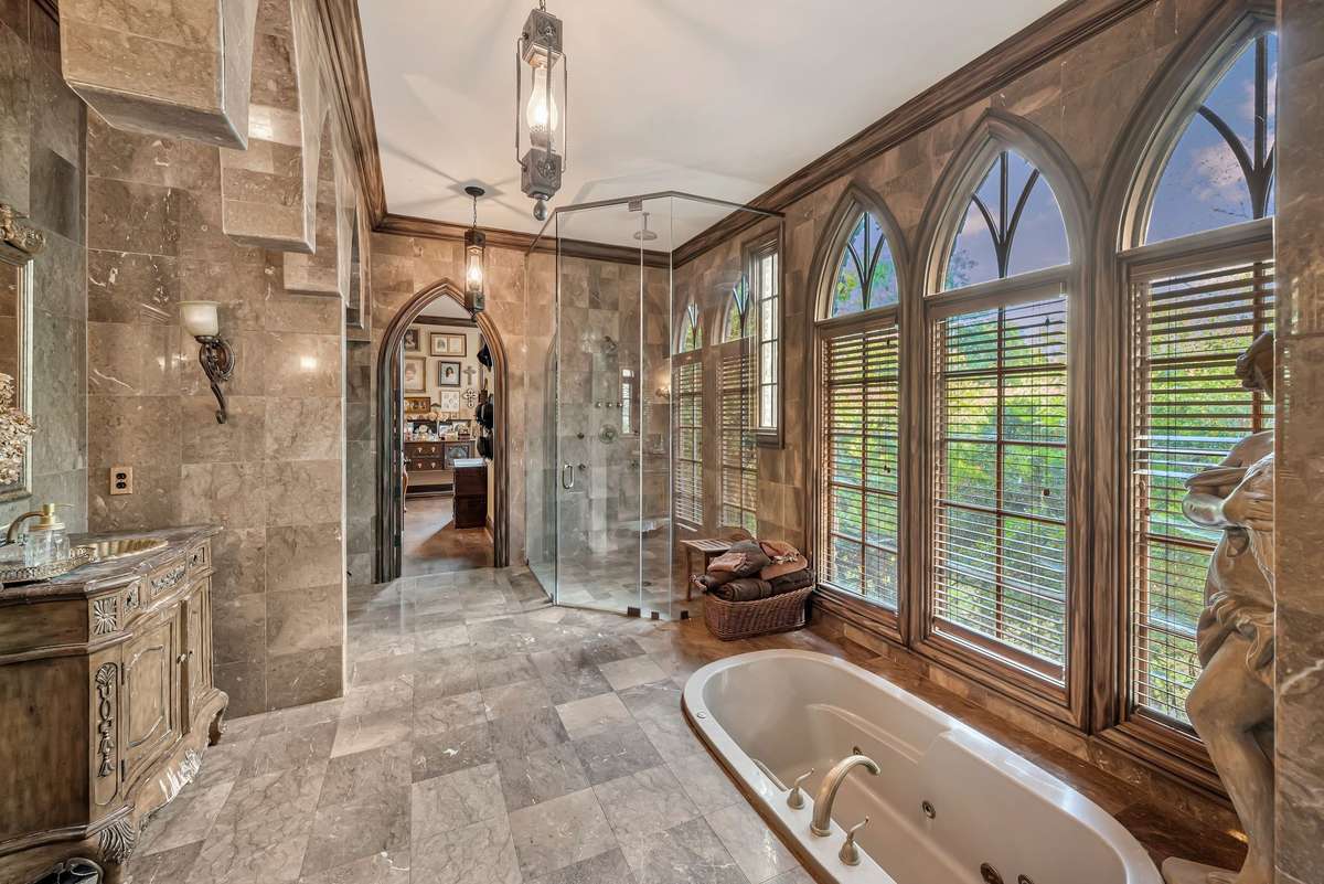 The Gothic main bathroom is a luxurious sanctuary wrapped in rich marble from floor to ceiling, arched openings overhead and tall arched windows and lead to the spacious closet and a discreet laundry area tucked away.