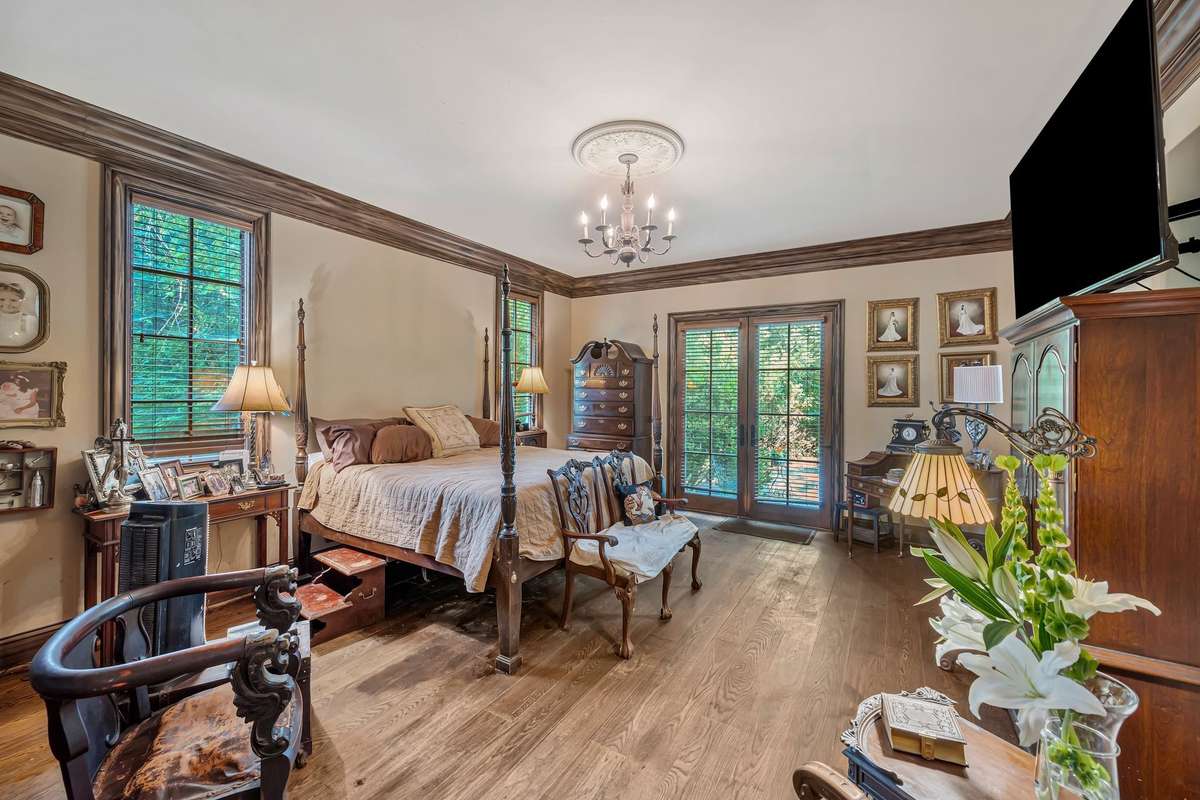 The main bedroom of this Gothic home is a romantic retreat with French doors framed in dark wood step into a private terrace that overlooks the kidney shaped pool