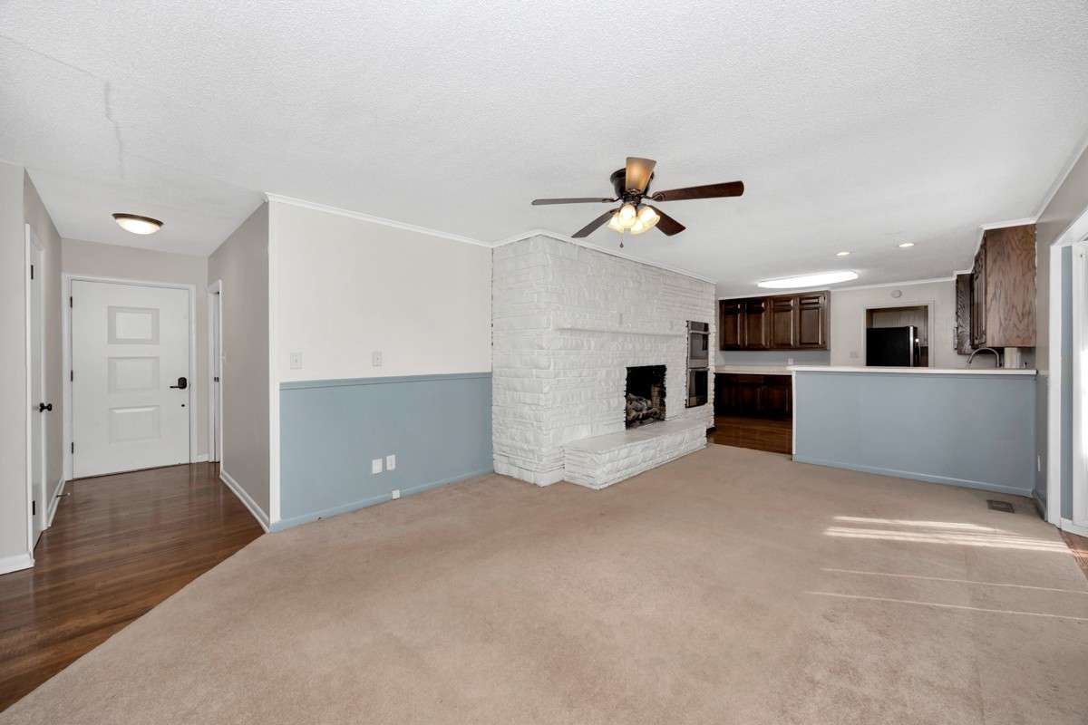 Den- carpet, crown molding, fireplace, ceiling fan