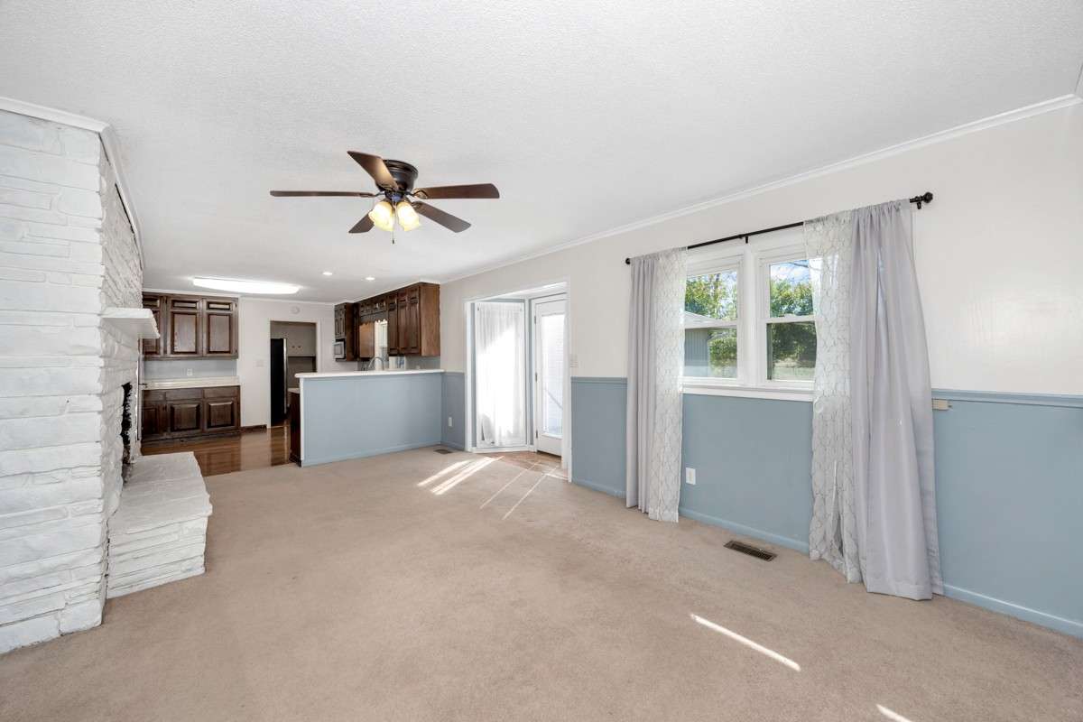 Den- carpet, crown molding, fireplace, ceiling fan