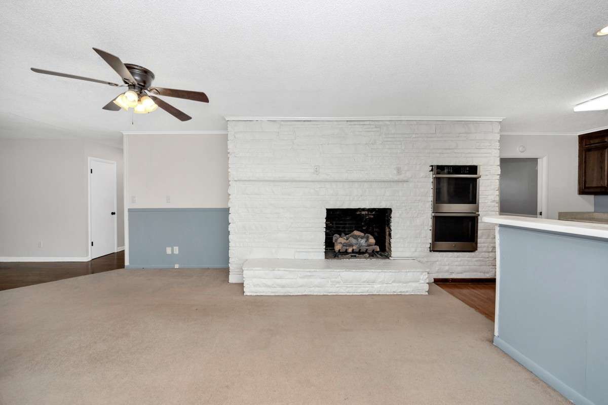 Den- carpet, crown molding, fireplace, ceiling fan