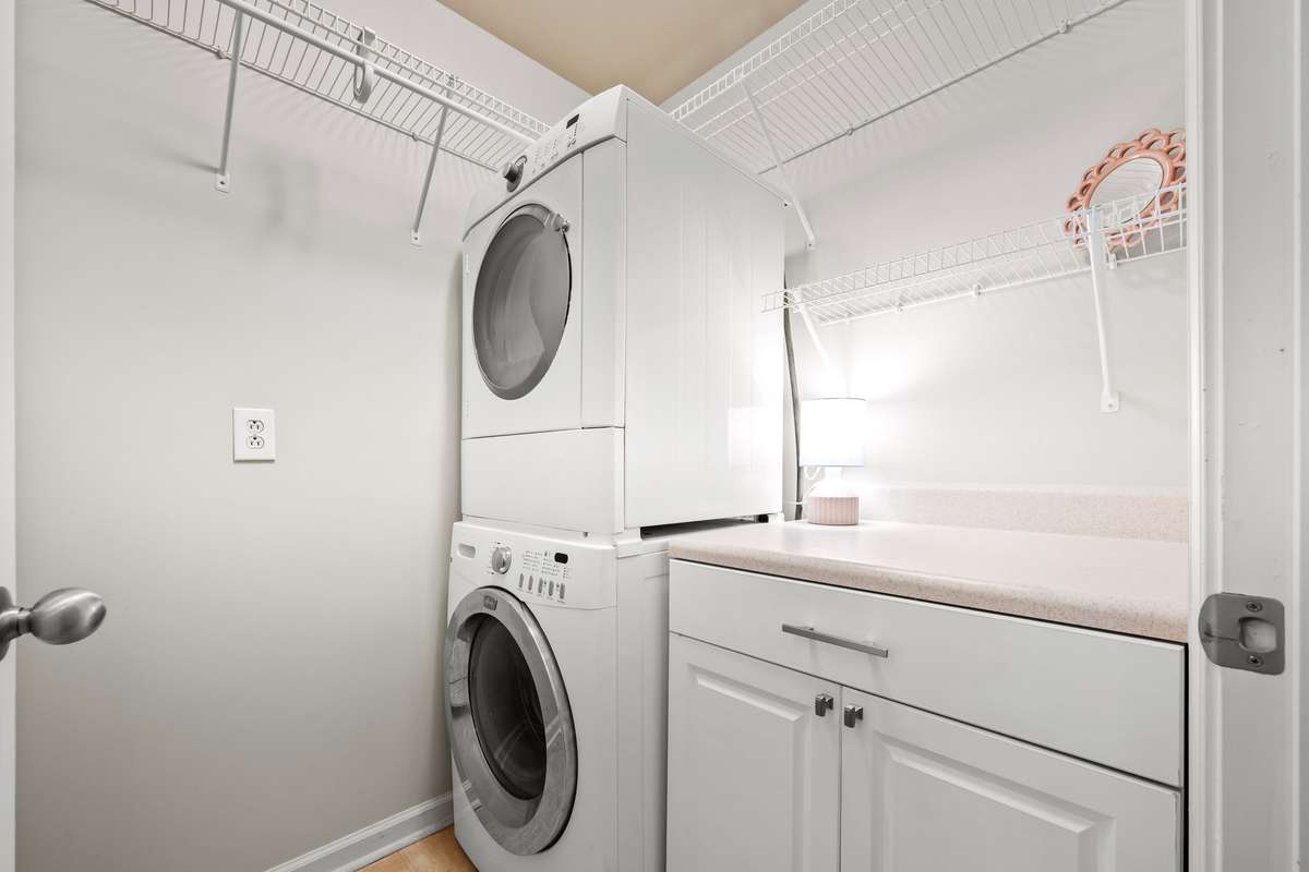 Laundry room with stackable washer and dryer that convey.  Cabinet offers perfect place to fold and hang clothes.