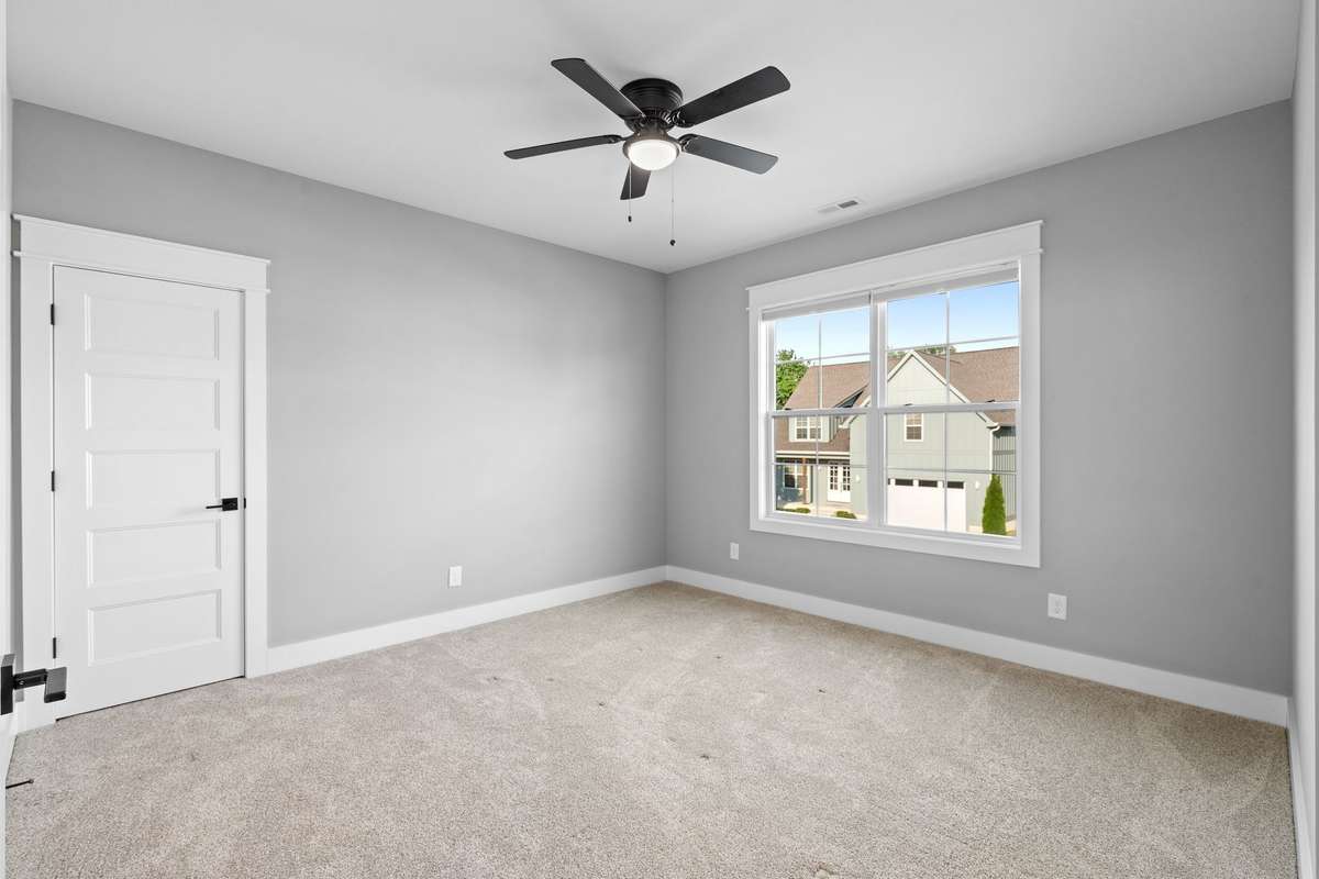 Spacious secondary bedroom with plush carpet, ceiling fan, and abundant natural light.
