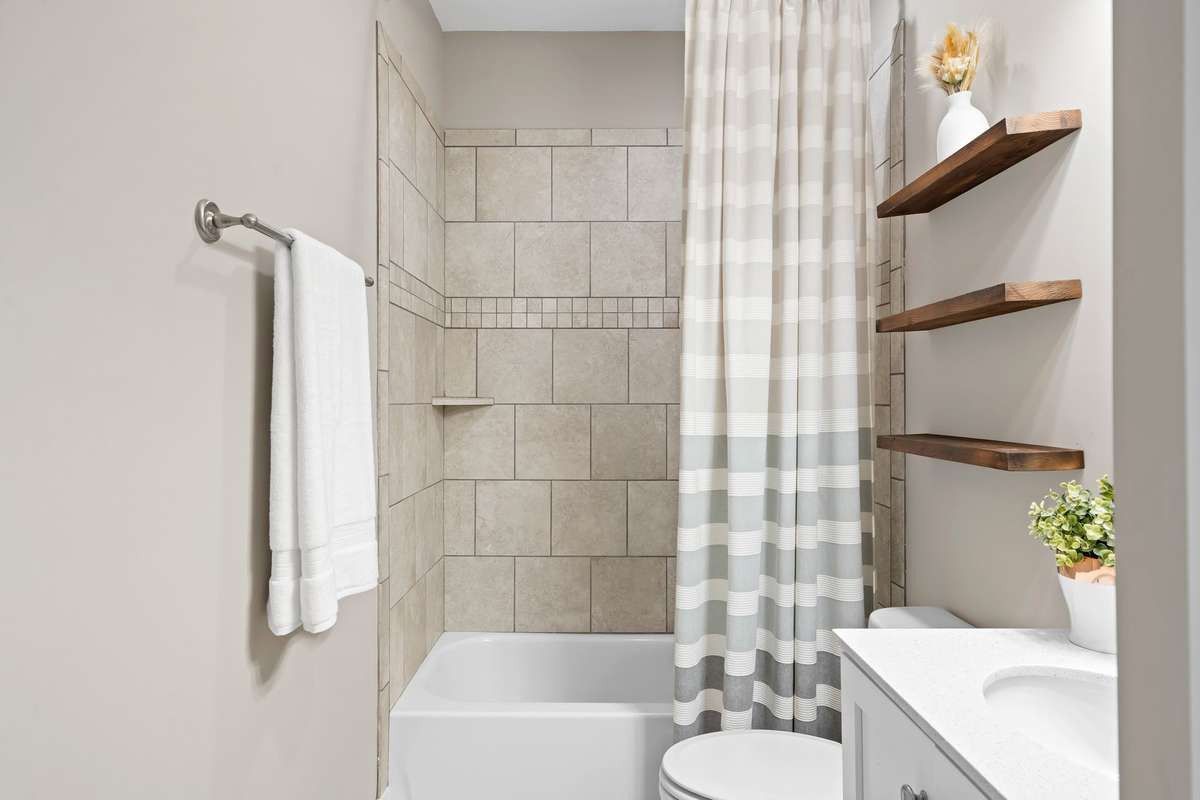 Full guest bathroom featuring tile surround tub and floating wood shelving for extra storage.