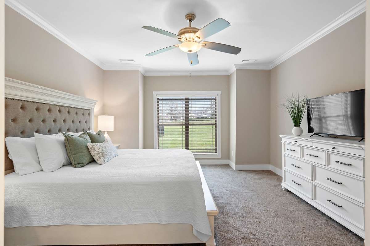 Spacious primary bedroom with neutral tones, crown molding, and large window bringing in natural light.