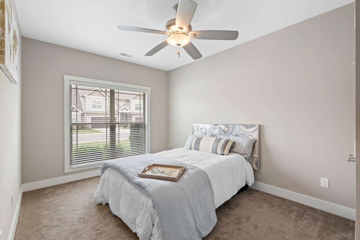 Comfortable guest bedroom with plush carpet, ceiling fan, and large window for natural light.