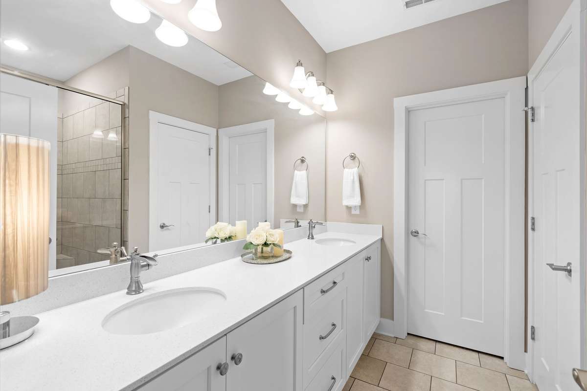 Primary bathroom featuring double vanity with quartz countertops, ample storage, and bright lighting.