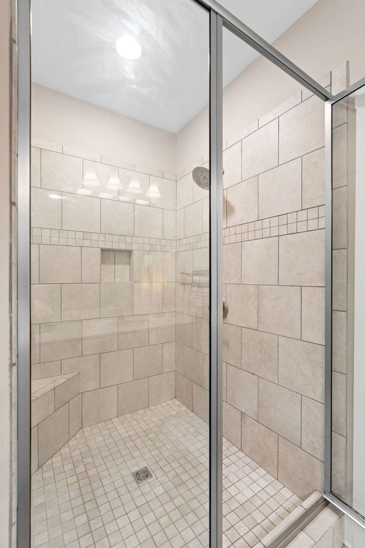 Walk-in tiled shower with glass enclosure, bench seating, and built-in niche.