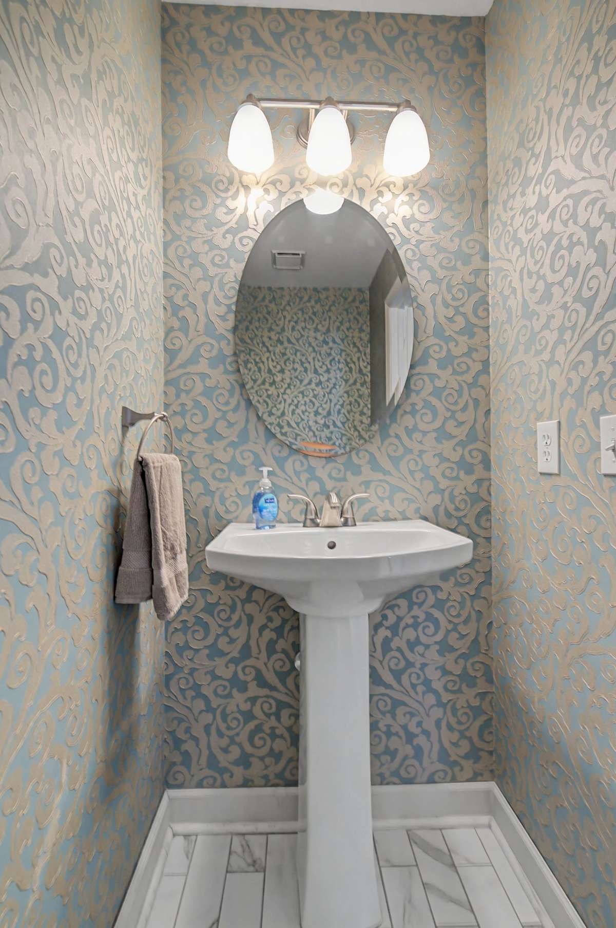 The half bath features a pedestal sink and stunning wallpaper, conveniently located on the lower level.