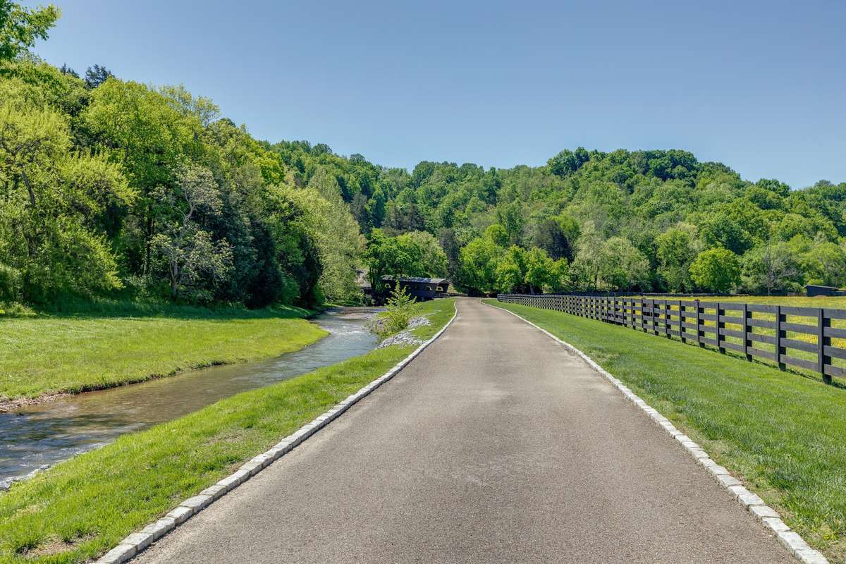 Curbed paved driveway hugs the Leipers Fork branch of S. Harpeth river, with level pasture on the other side