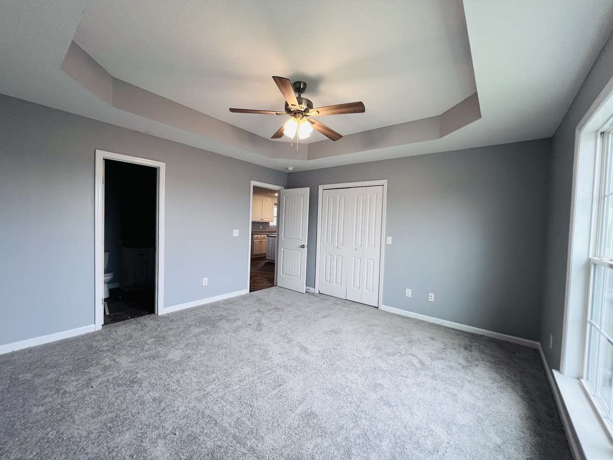 Primary bedroom with a ceiling fan and trey ceiling