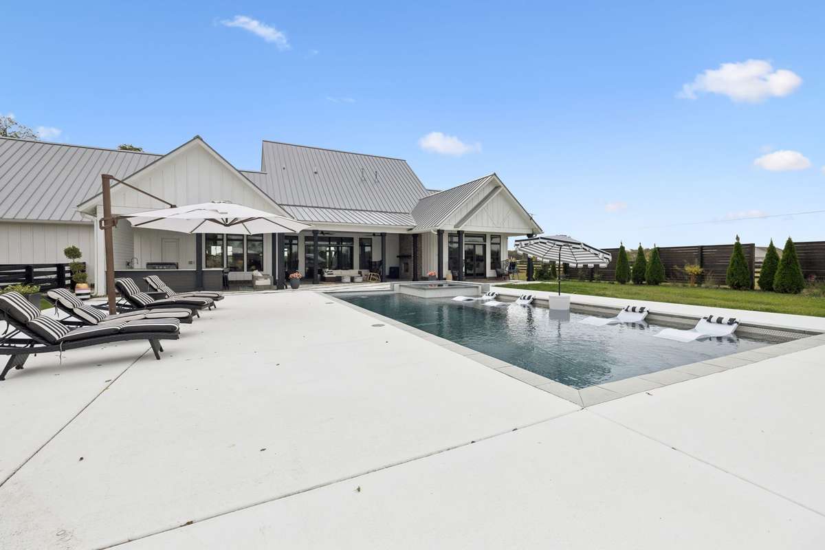 Striking modern farmhouse exterior with metal roof, covered outdoor living spaces, and panoramic pasture views.