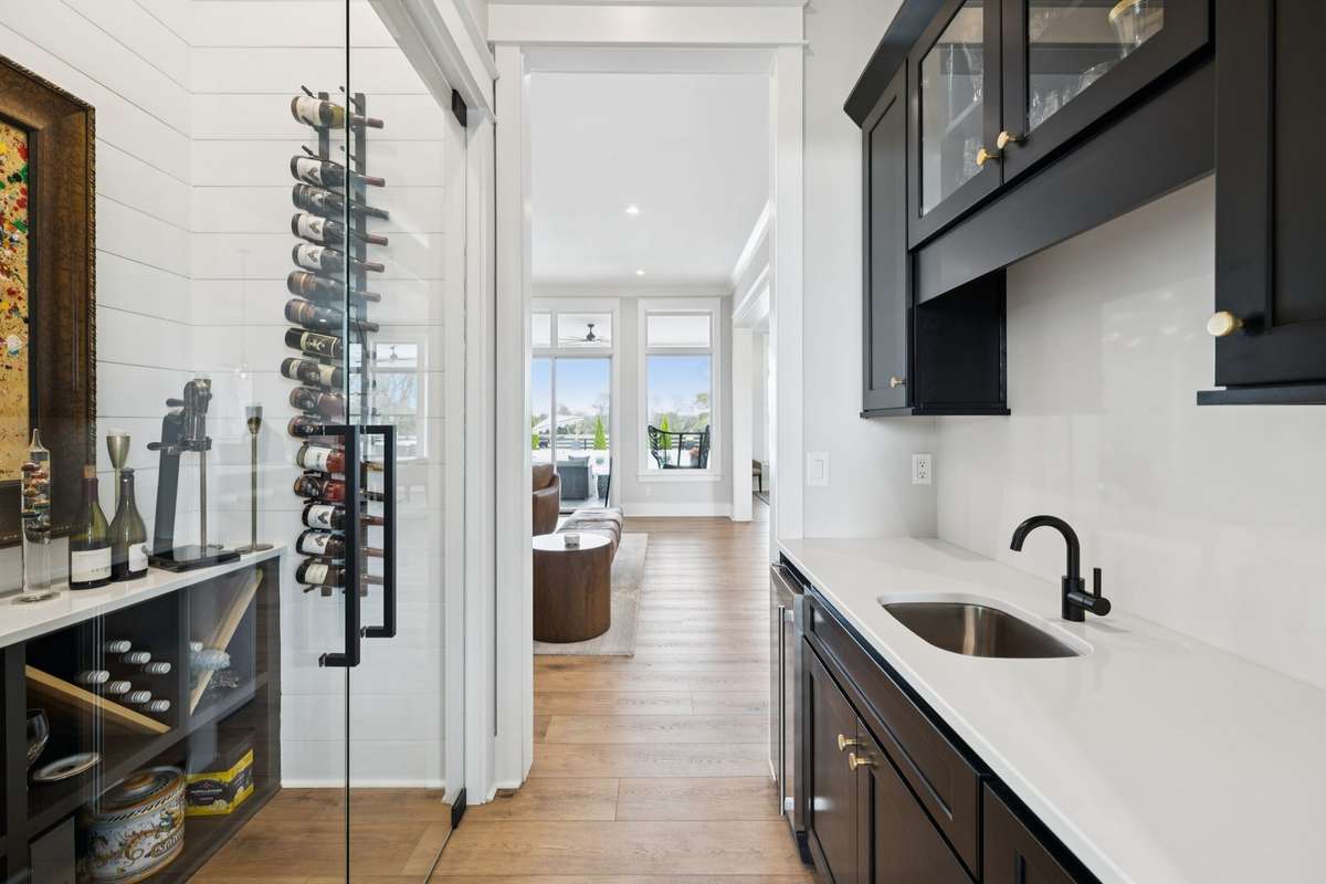 Built-in wet bar with quartz countertops, sink, and custom cabinetry sits beside a glass-enclosed wine display. Ideal for entertaining, this space offers convenient storage and a seamless connection to the main living areas.