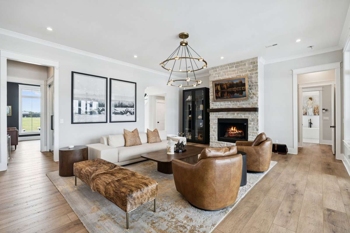 Inviting living room with stone fireplace, wood mantel, and open sightlines to adjoining spaces. Wide-plank flooring and neutral finishes create a warm, cohesive setting ideal for entertaining or relaxed evenings at home.