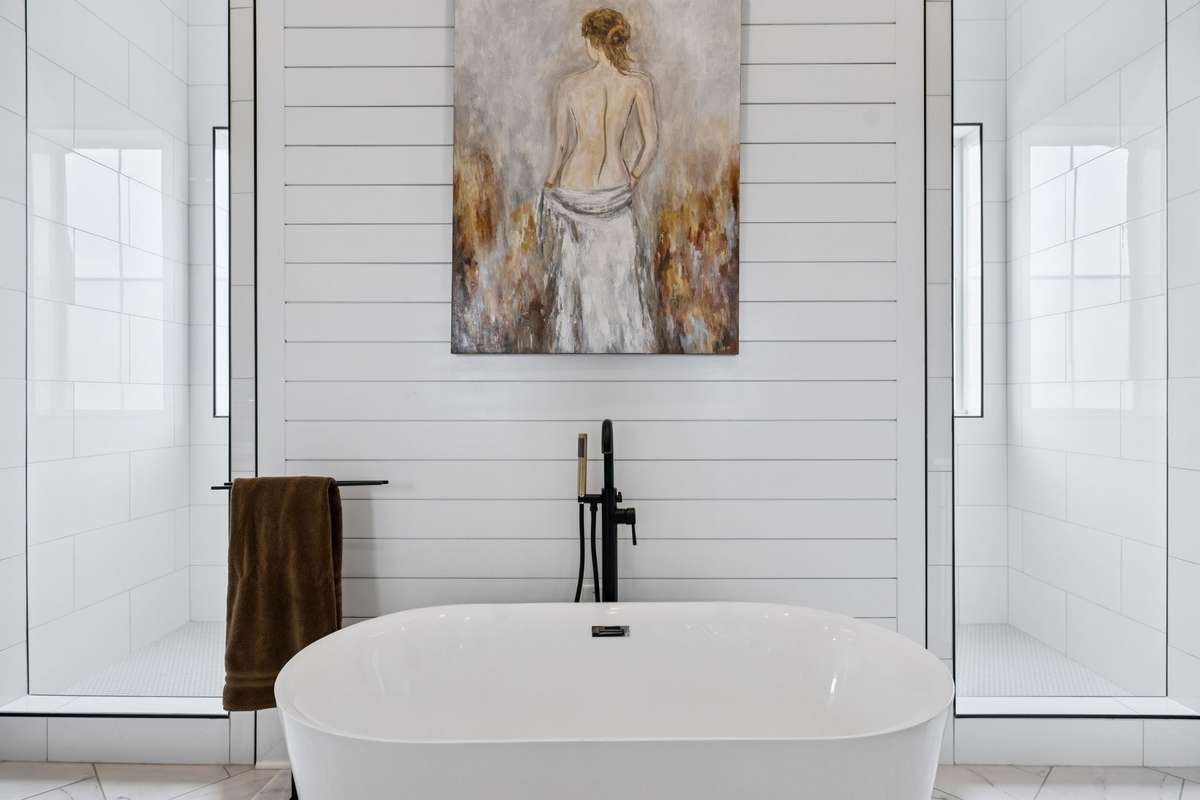 Freestanding soaking tub set before an expansive walk-in shower with dual glass enclosures. Thoughtfully designed layout offers both a spa-like retreat and everyday functionality within the primary bath.