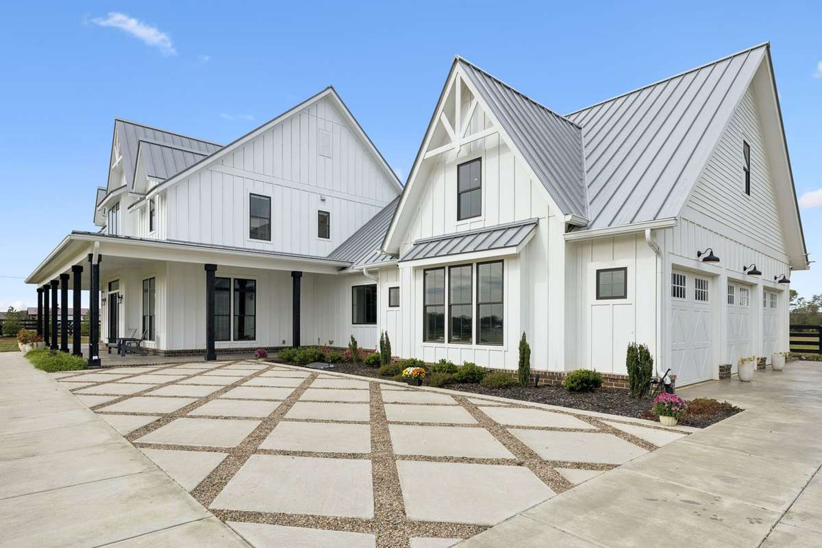 Spacious side entry with three-car garage and extended concrete drive provides ample parking for guests and daily living. Board-and-batten exterior, metal roof accents, and covered porch details highlight the home’s thoughtful design & functionality.