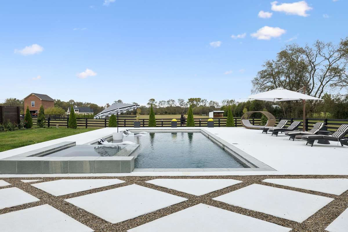 Custom in-ground pool with tanning ledge and integrated spa, surrounded by expansive hardscaping and open countryside views.