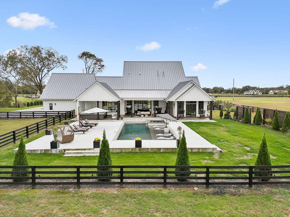 Stunning modern farmhouse exterior overlooking a custom in-ground pool and expansive fenced pasture. Designed for seamless indoor-outdoor living with covered entertaining spaces and panoramic countryside views.
