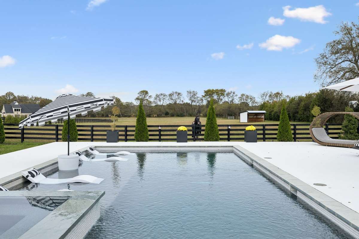 Custom in-ground pool with tanning ledge and integrated spa, surrounded by expansive hardscaping and open countryside views.