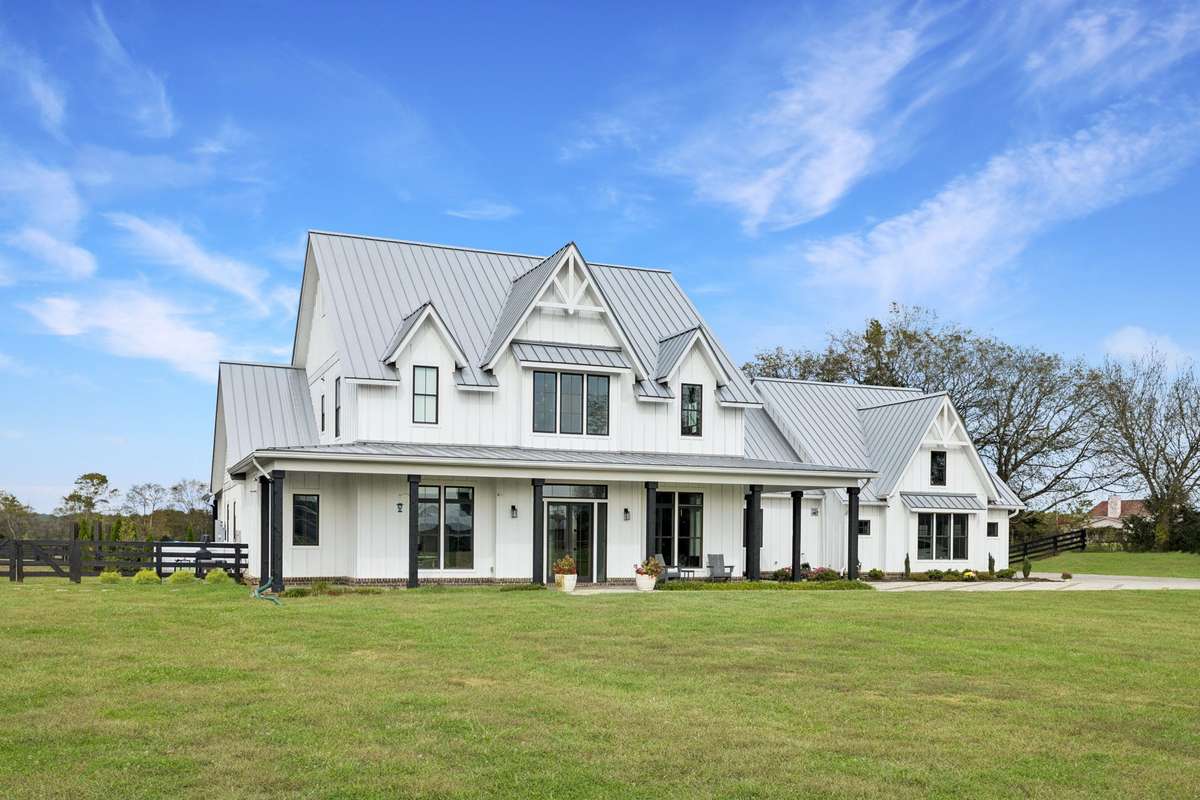 Classic modern farmhouse design featuring board-and-batten siding, standing seam metal roof, and expansive covered porches. Multiple outdoor seating areas overlook level acreage, offering seamless indoor-outdoor living and space to enjoy.