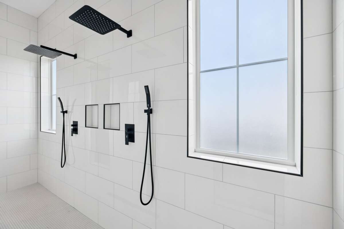 Expansive walk-in shower with dual rain shower heads, handheld fixtures, and sleek tile surround. Spacious design and natural light create a luxurious, spa-like experience within the primary bath.