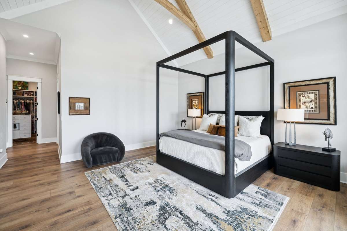 Spacious main level primary suite featuring vaulted ceilings with exposed beams and wide-plank floors. Generous layout offers room to unwind, with direct access to outdoor living and a large walk-in closet just beyond.