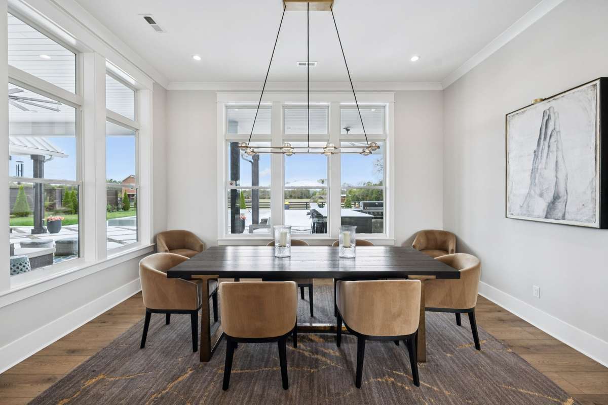 Dining area surrounded by windows overlooking the pool and patio. Clean lines, modern lighting, and open flow to the kitchen create an inviting space for everyday meals or hosting gatherings with views of the landscaped grounds.