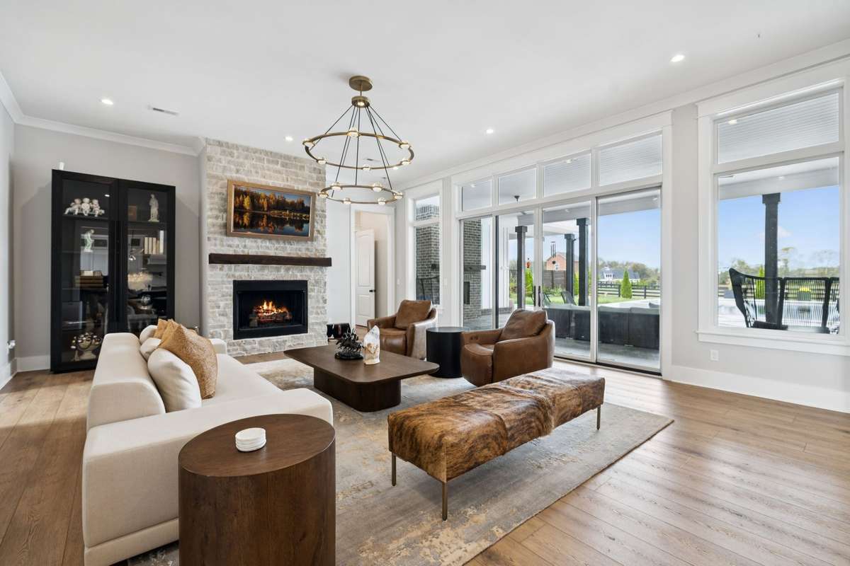 Open-concept living area centered around a stone fireplace with wood mantel. Expansive windows and sliding doors fill the space with natural light and connect seamlessly to the covered outdoor living area and pool beyond.