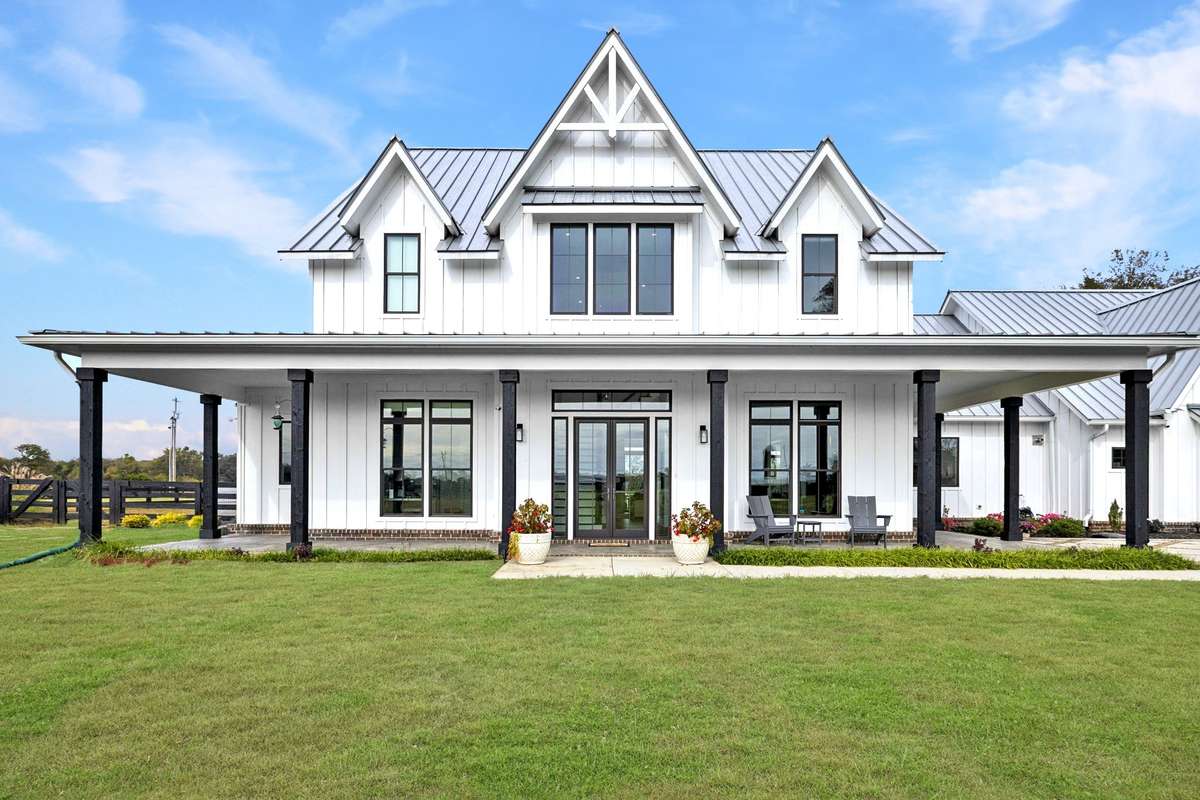 Modern farmhouse exterior with metal roof, board-and-batten siding, and a covered porch designed for outdoor living. Expansive windows invite natural light, while the flat lawn and fenced acreage offer space to relax, entertain, and enjoy!
