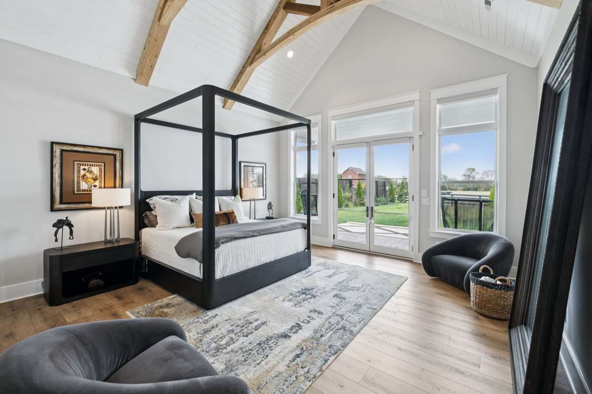 Main level primary suite with vaulted ceilings and exposed beams, creating an open, airy retreat. French doors lead to the patio and frame peaceful views of the surrounding acreage, blending indoor comfort with outdoor living.