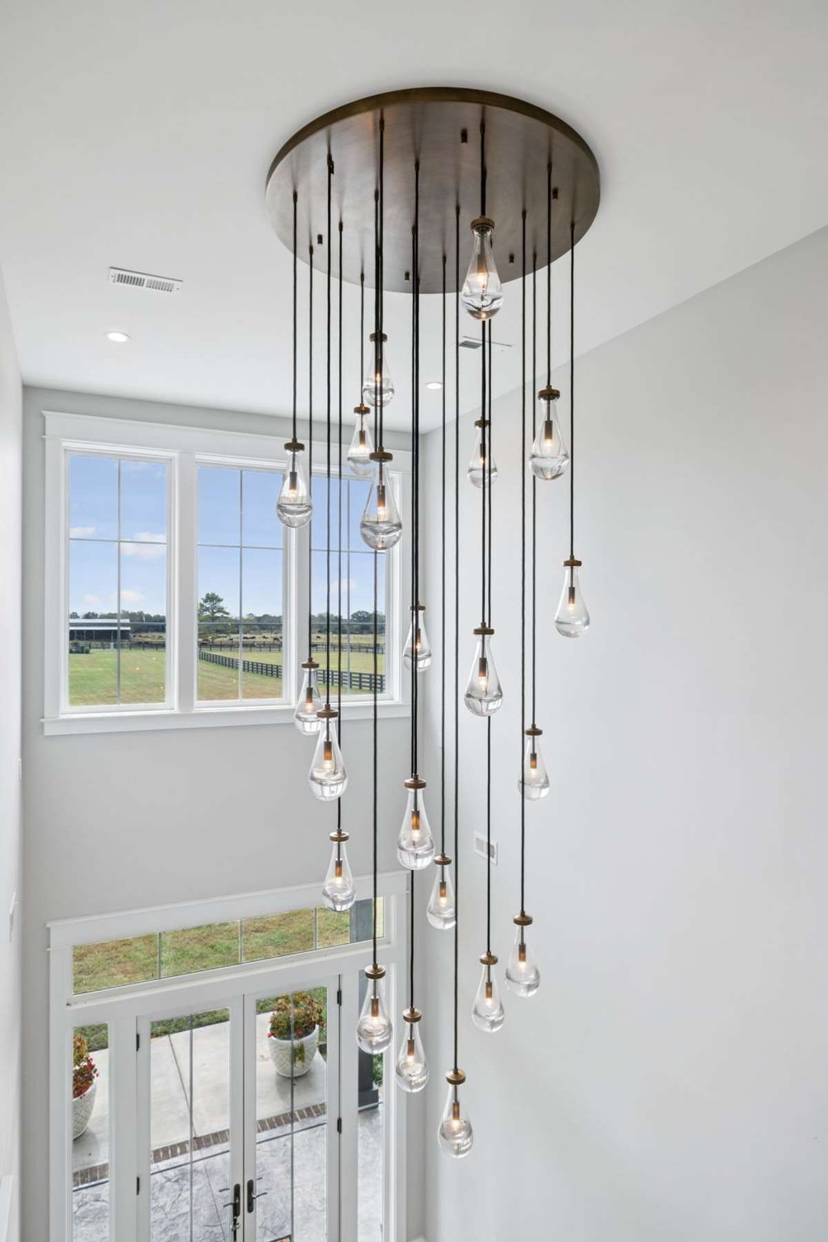 Statement Restoration Hardware chandelier cascades from the two-story ceiling, serving as a striking focal point in the foyer. Suspended glass pendants create a sculptural effect while enhancing the natural light from expansive windows.