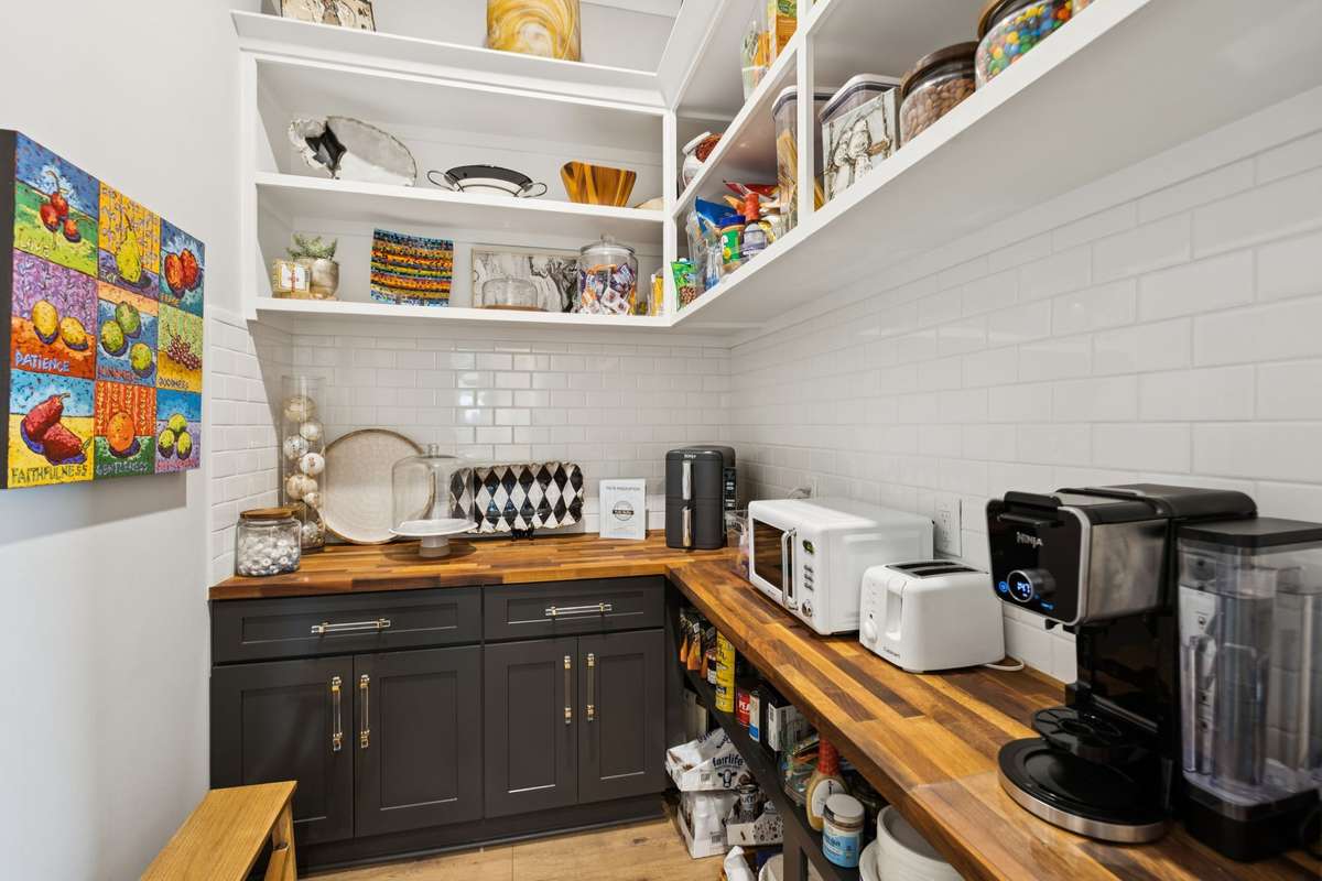 Walk-in pantry with butcher block counters, open shelving, and subway tile backsplash. Ample storage and prep space keep small appliances organized while supporting effortless everyday cooking and entertaining.