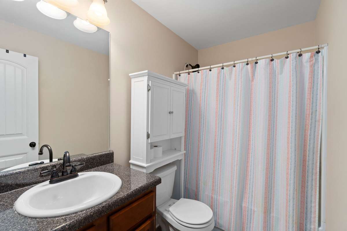Full secondary bathroom featuring a wood vanity with dark granite countertop, sink, tub and shower combo, and toilet, providing comfortable accommodations for family members or guests.
