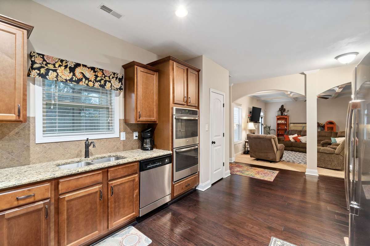 Kitchen sink area with granite countertops, tile backsplash, stainless appliances, and a direct sightline into the living room, perfect for keeping an eye on the family while cooking.
