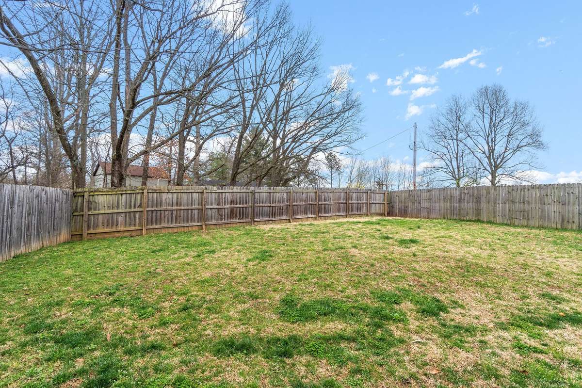 Wide-angle view of the backyard showing the generous open lawn, full privacy fencing on all sides, and the impressive two-story rear elevation of the home with dual chimneys.