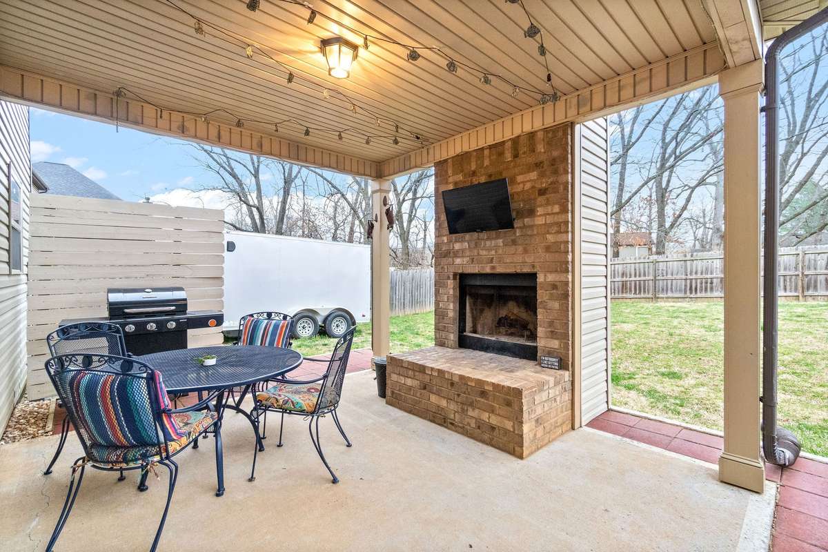 Spacious covered back deck featuring a wood-burning outdoor fireplace, mounted flat-screen TV, and ample space for outdoor dining and entertaining — perfect for year-round enjoyment.