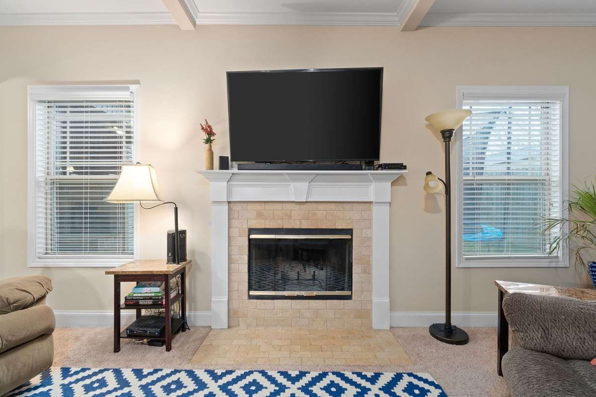 Cozy living room fireplace with tile surround and white mantle, flanked by windows that fill the space with natural light and creating the perfect focal point in the main living area.
