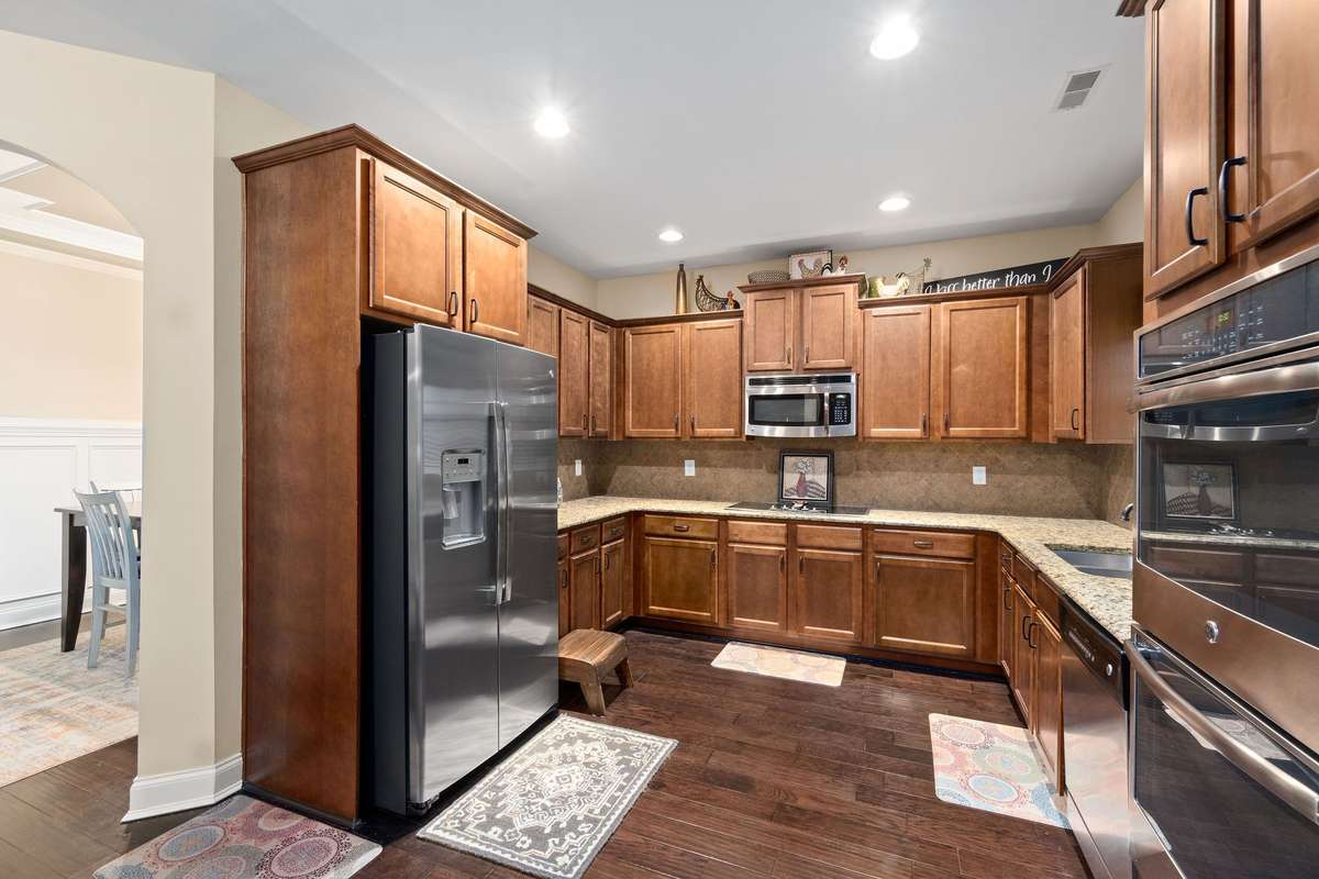Open-concept kitchen with ample wood cabinetry, granite countertops, stainless steel appliances including a cooktop and double ovens, and seamless flow into the dining and living areas.