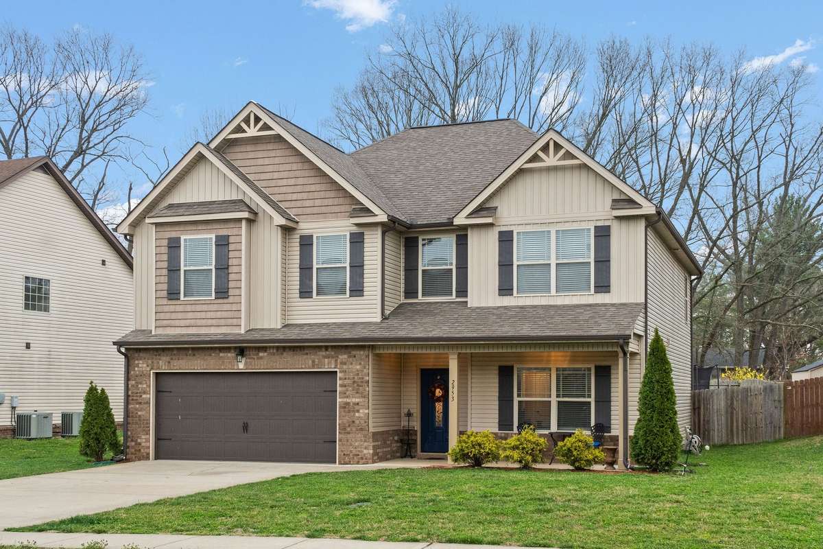 Outdoor living area with brick columns framing the covered deck and full brick fireplace with TV, overlooking the open green backyard within a fully privacy-fenced space.
