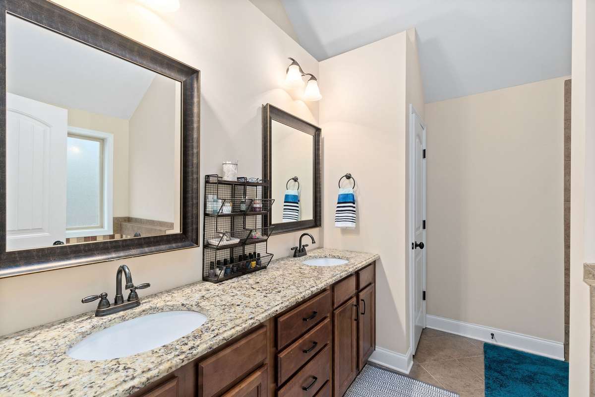 Spa-inspired primary en suite bathroom with a double vanity, granite countertops, dark wood cabinetry, and large framed mirrors, offering a luxurious daily retreat for the homeowners.