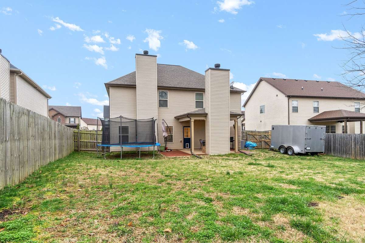 Rear exterior view showing the full two-story back of the home, spacious green backyard, covered deck access, and fully privacy-fenced yard, ideal for outdoor recreation and entertaining.