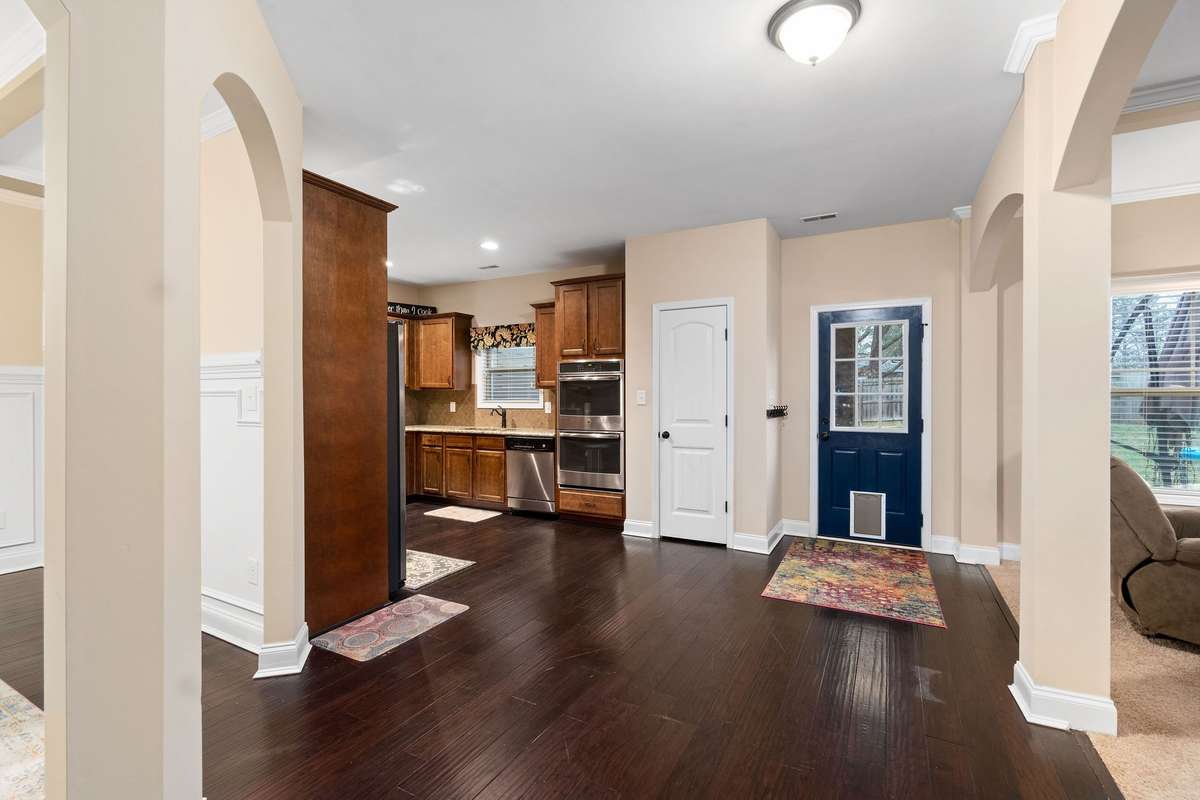 Grand entry foyer featuring rich hardwood floors, elegant arched doorways, wainscoting, and an open view through to the kitchen — making a wonderful first impression upon arrival.