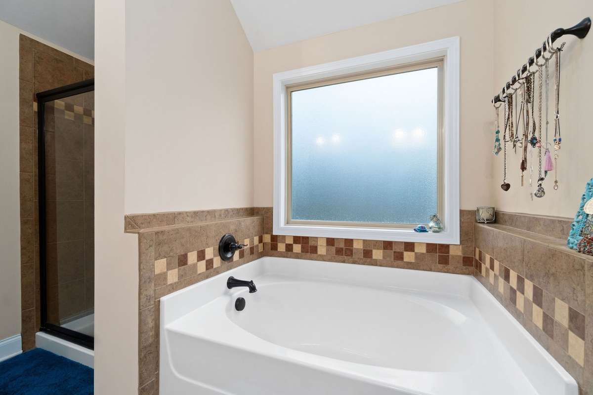 Primary bathroom soaking tub with elegant tile surround, frosted privacy window, and a separate walk-in shower, completing the spa-like en suite experience of the primary bedroom.