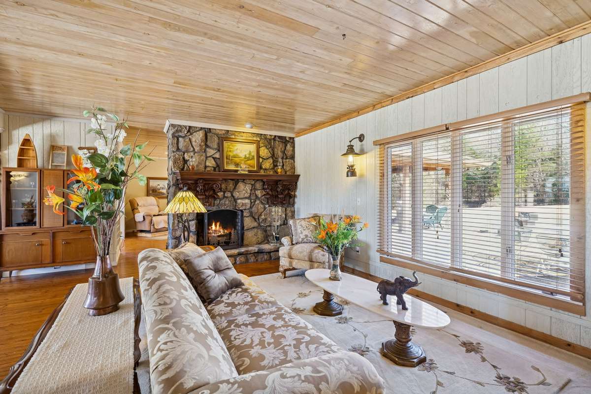 One of multiple living spaces featuring a stunning floor-to-ceiling stone fireplace, beautiful wood plank ceiling, and expansive windows overlooking the property. 1372 Short Mountain Rd, McMinnville, TN 37110