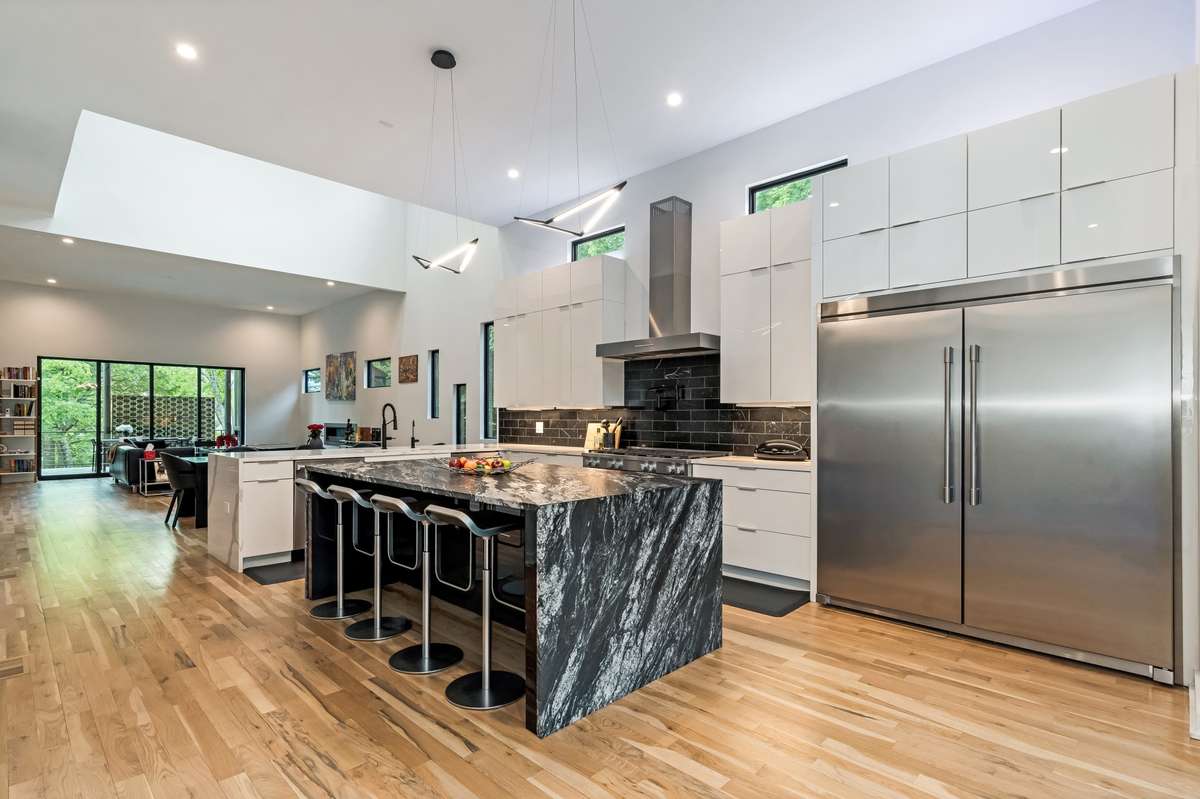 This chef-inspired kitchen showcases a leathered polished-granite waterfall island with bar seating, highlighted by two sleek Koncept Z-Bar Bird pendant lights.