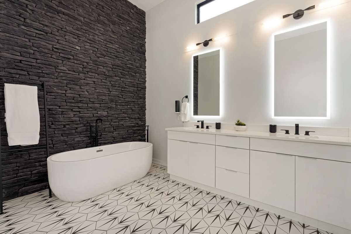 The spa-inspired primary bath offers an extended dual vanity, a relaxing soaking tub, and a striking floor-to-ceiling stone wall accent.