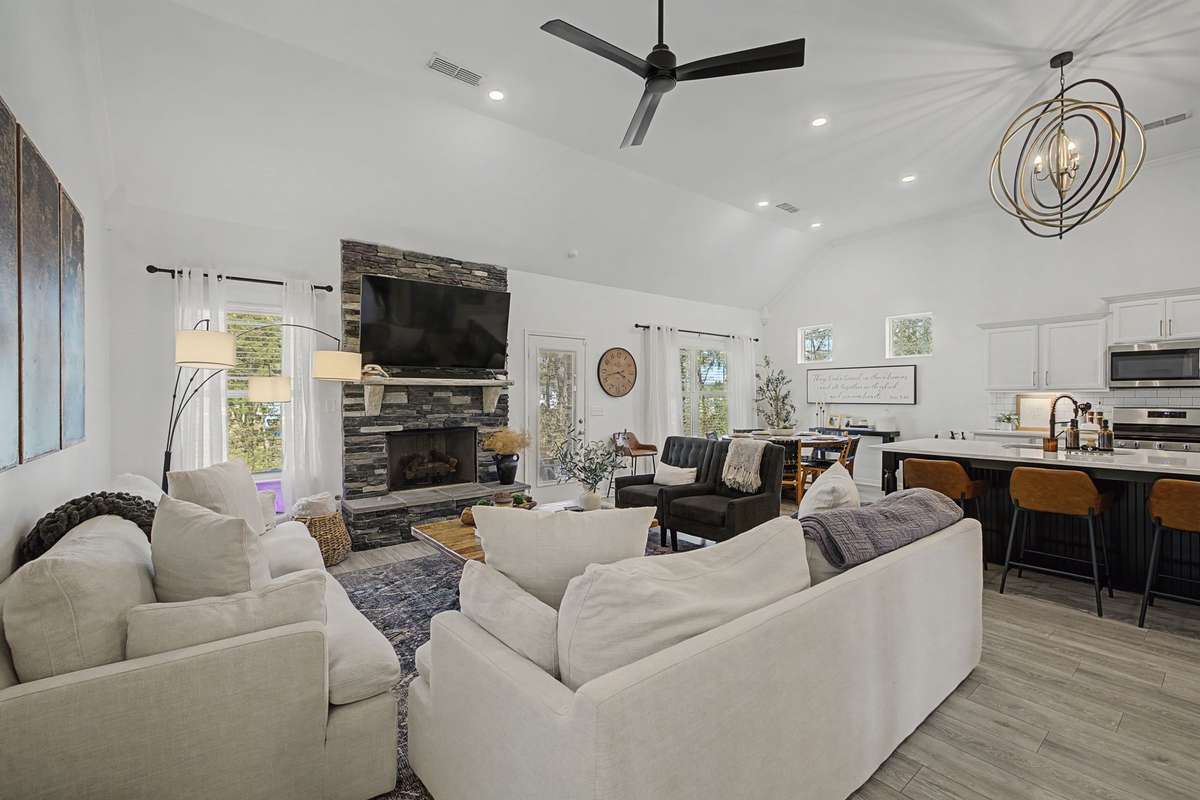 Bright and airy! Great Room with Stacked Stone Gas Fireplace, updated lighting and Vaulted Ceilings. View of the Kitchen and Dining Area in the Background.